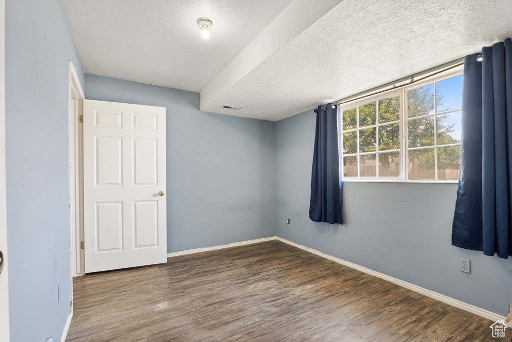 Unfurnished room with a textured ceiling, wood finished floors, and baseboards