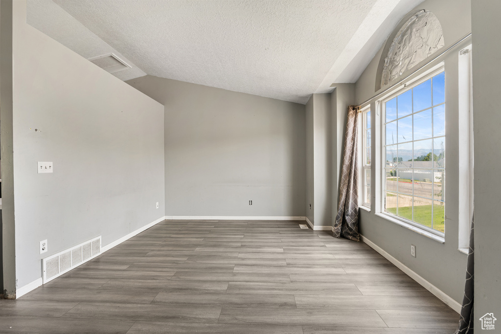 Unfurnished room with a textured ceiling, vaulted ceiling, wood finished floors, and baseboards