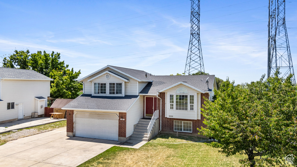 Split level home with brick siding, concrete driveway, a front lawn, roof with shingles, and a garage
