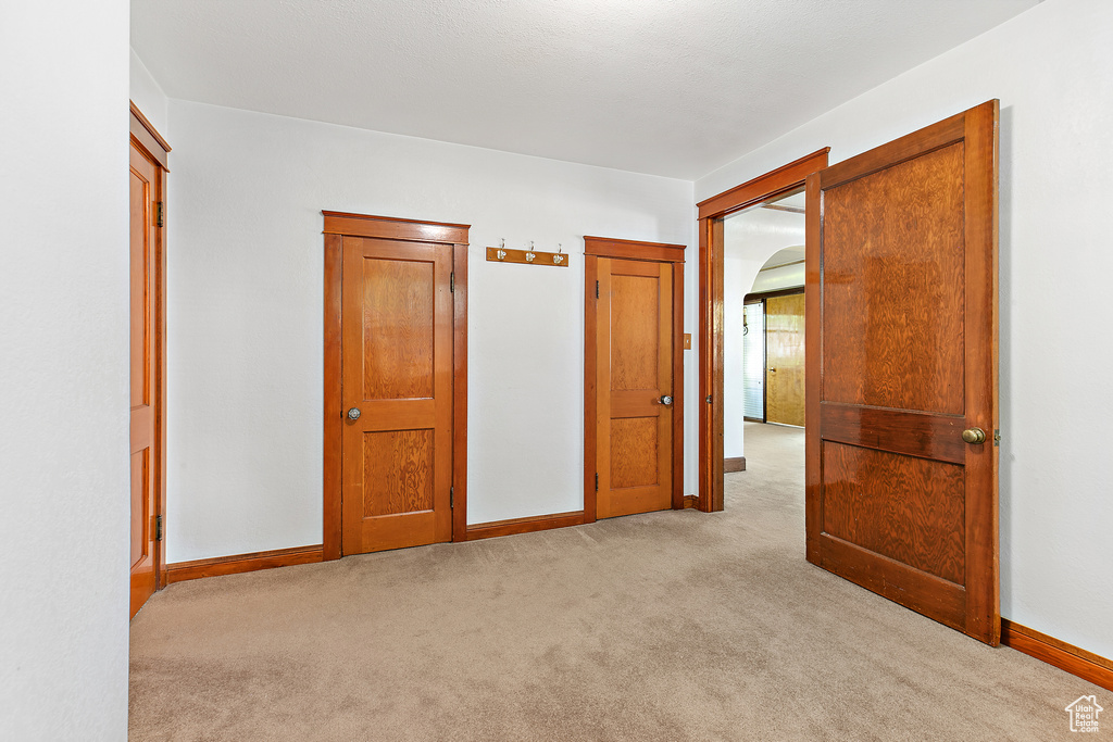 Unfurnished bedroom featuring light carpet, baseboards, and arched walkways