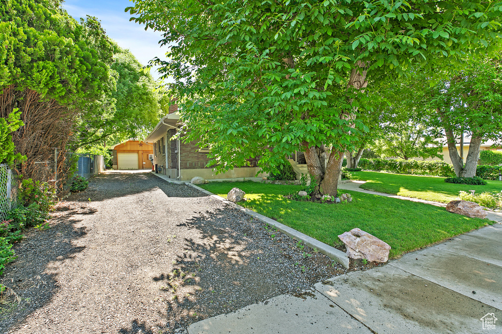 View of property hidden behind natural elements with gravel driveway, an outbuilding, and a chimney
