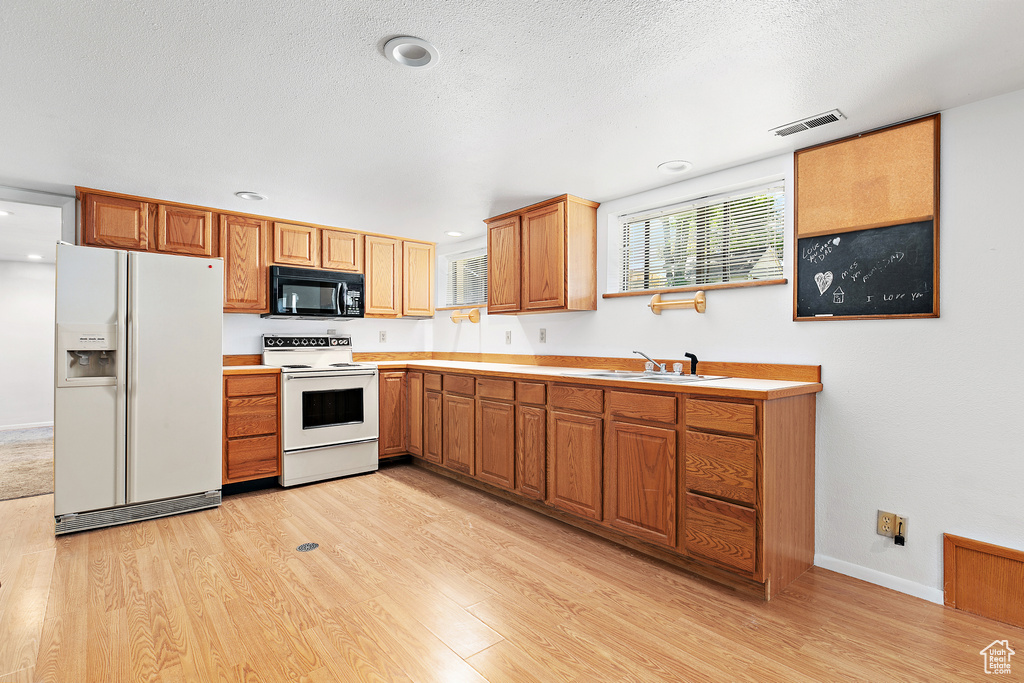 Kitchen featuring white appliances, light wood-style floors, a sink, recessed lighting, and a textured ceiling