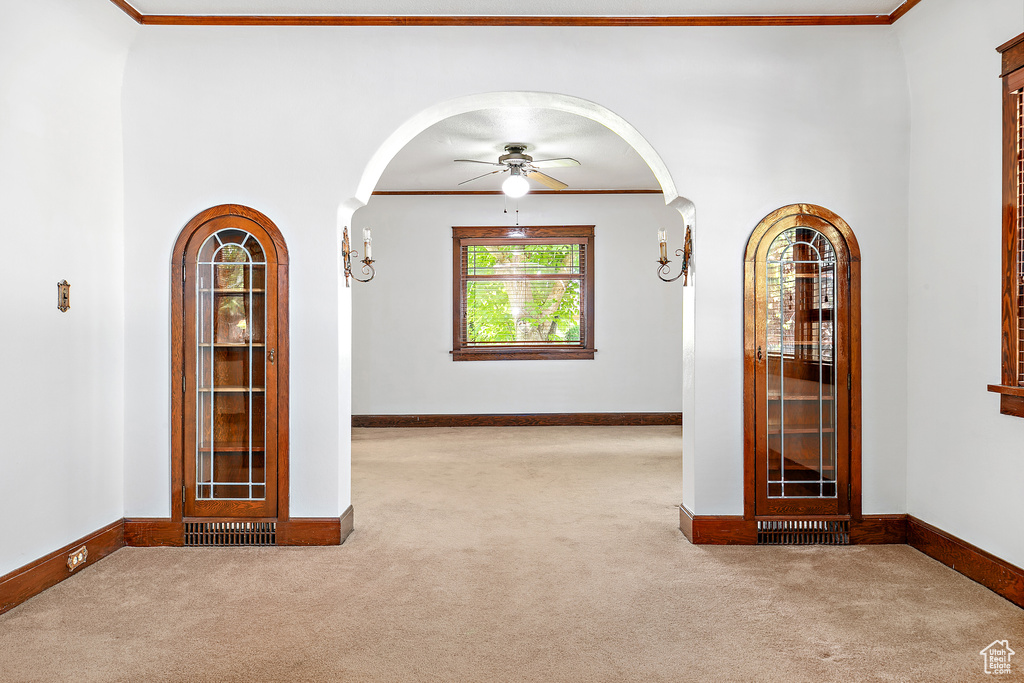 Spare room with carpet, arched walkways, ceiling fan, crown molding, and baseboards