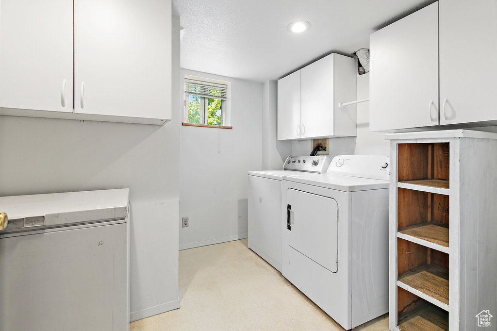 Washroom featuring washing machine and dryer, cabinet space, baseboards, and light flooring