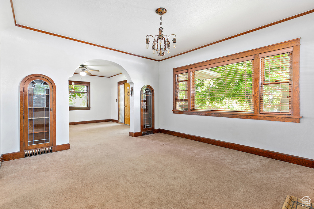 Carpeted empty room featuring baseboards, crown molding, arched walkways, and a chandelier