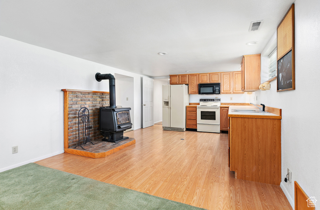 Kitchen featuring white appliances, a sink, a wood stove, light countertops, and light wood finished floors