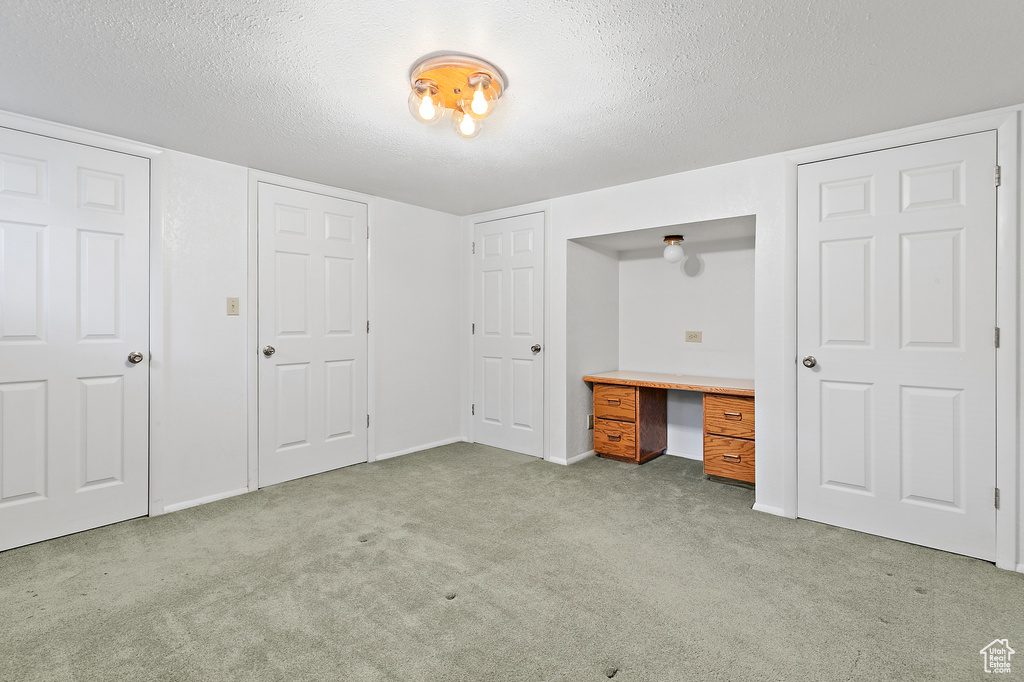Unfurnished bedroom with carpet flooring, a textured ceiling, a desk, and baseboards