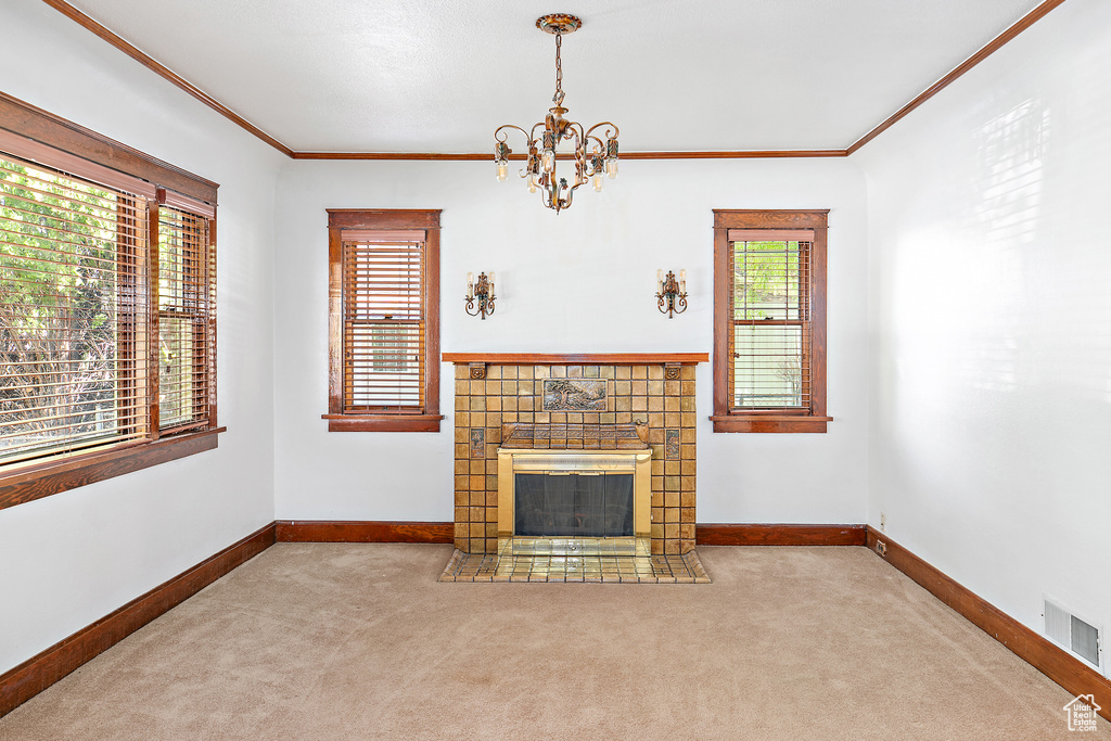 Unfurnished living room with carpet flooring, crown molding, a chandelier, a tile fireplace, and baseboards