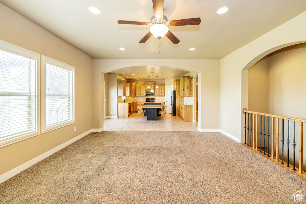 Unfurnished living room with light colored carpet, arched walkways, ceiling fan, recessed lighting, and baseboards