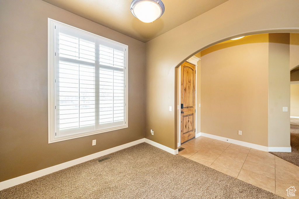 Tiled spare room featuring arched walkways, carpet flooring, and baseboards