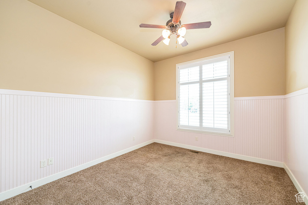 Carpeted empty room with a wainscoted wall, ceiling fan, and vaulted ceiling