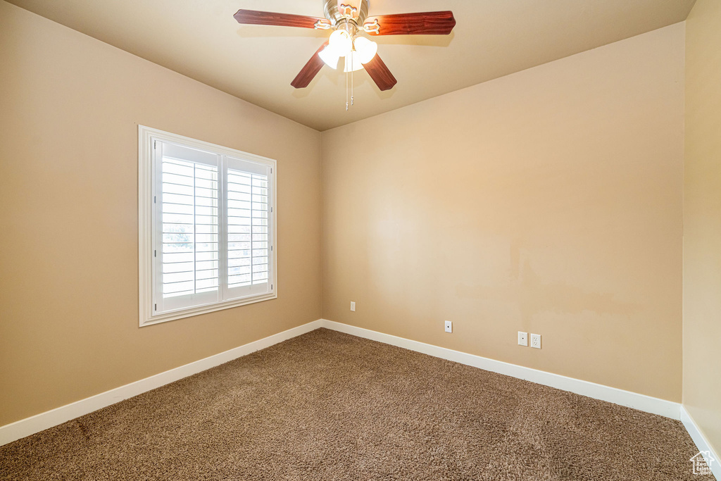 Unfurnished room with dark colored carpet, baseboards, and ceiling fan