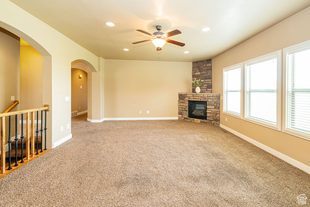 Unfurnished living room with a ceiling fan, recessed lighting, a fireplace, arched walkways, and carpet floors