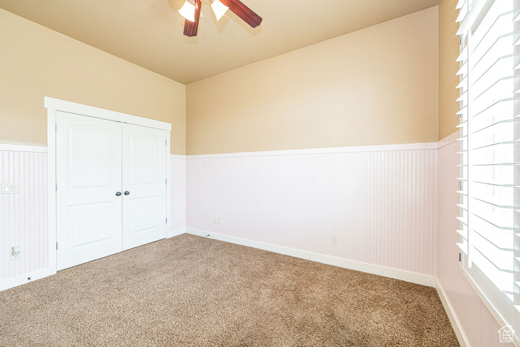 Unfurnished bedroom with wainscoting, carpet, a closet, and ceiling fan