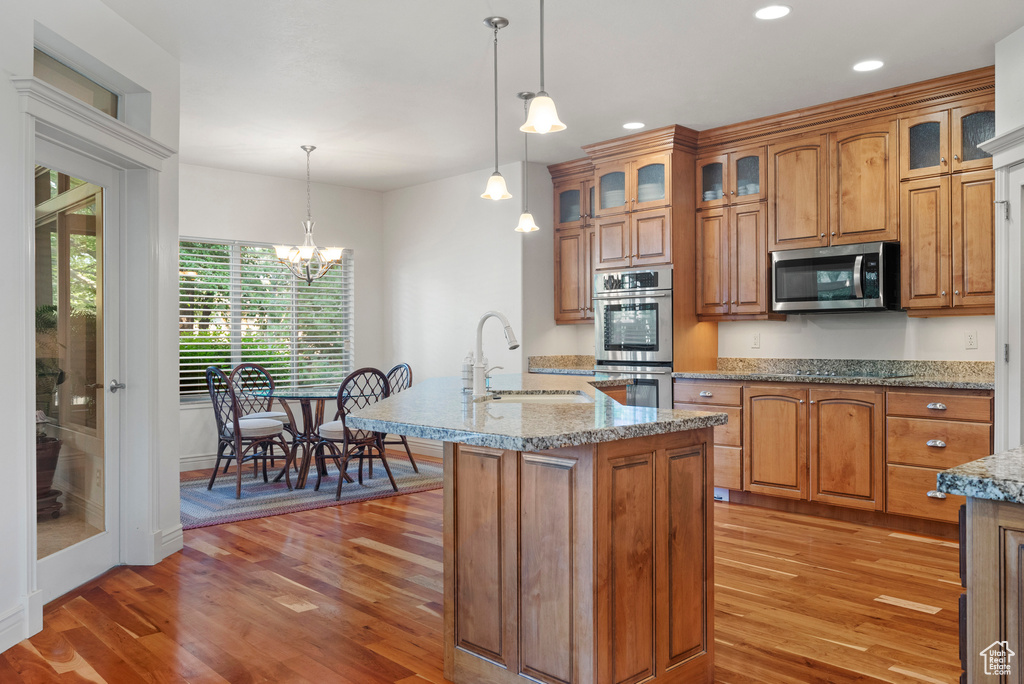 Kitchen with stainless steel appliances, a sink, light wood-type flooring, brown cabinetry, and recessed lighting