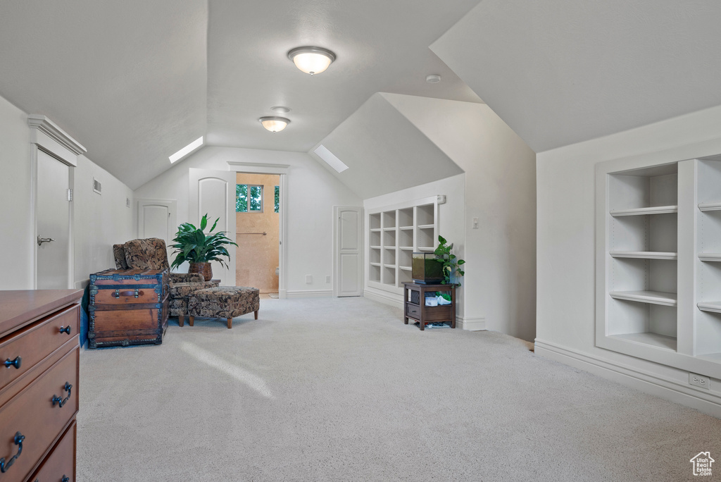 Living area featuring built in shelves, vaulted ceiling, carpet floors, and baseboards