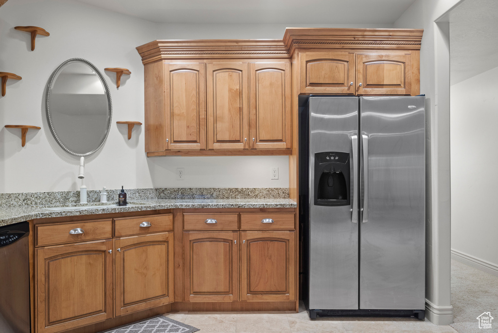 Kitchen with appliances with stainless steel finishes, a sink, light stone countertops, and brown cabinetry