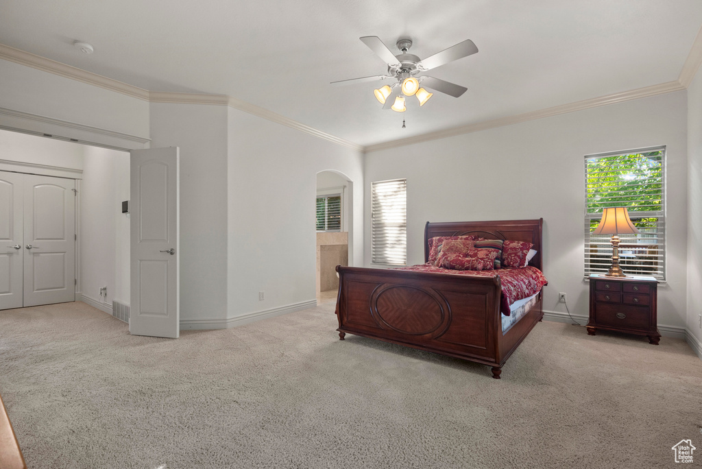 Carpeted bedroom with arched walkways, crown molding, baseboards, and a ceiling fan