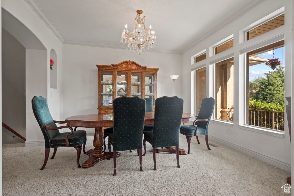 Dining space with carpet, a chandelier, arched walkways, ornamental molding, and baseboards