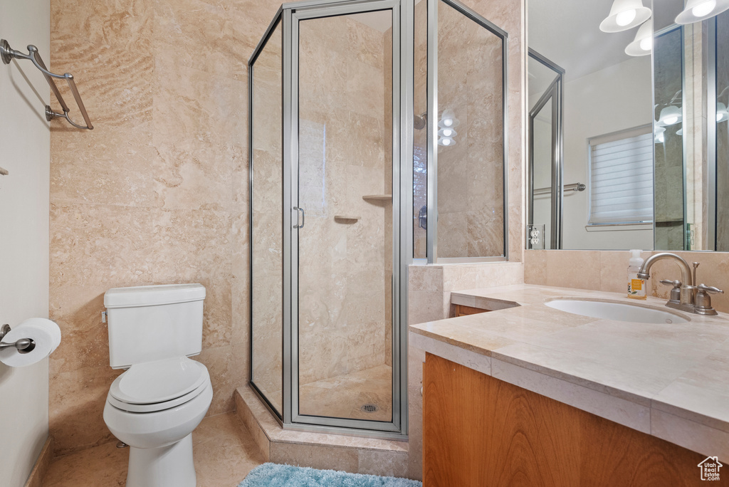 Bathroom with vanity, a stall shower, toilet, tile walls, and tile patterned floors