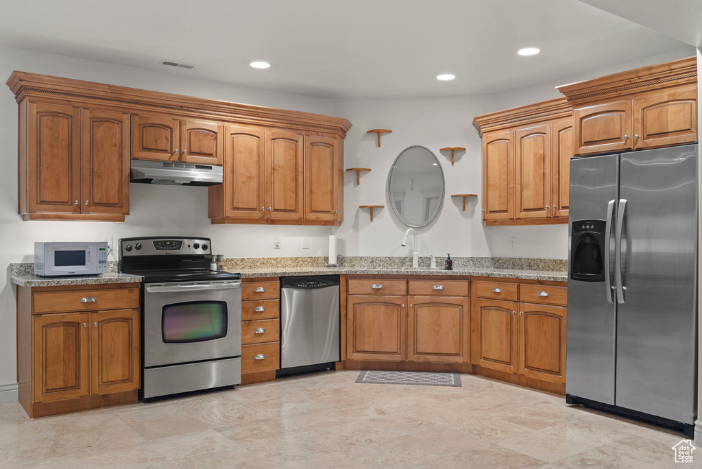 Kitchen with appliances with stainless steel finishes, under cabinet range hood, light stone counters, brown cabinetry, and recessed lighting