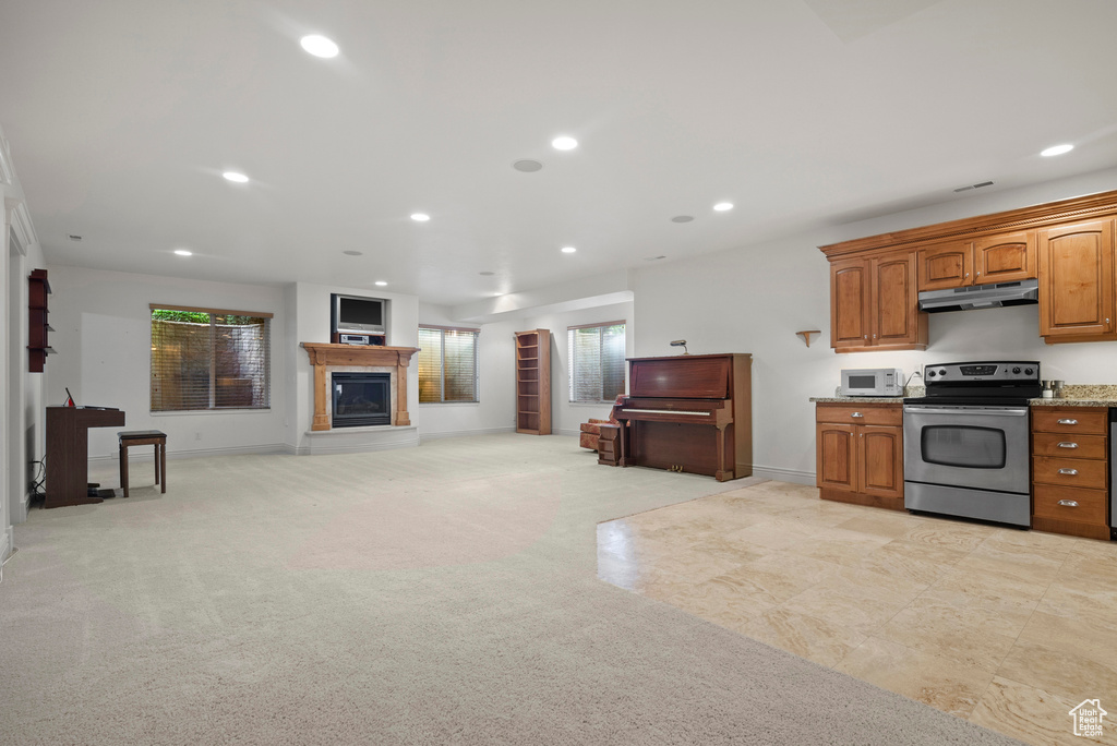 Kitchen featuring stainless steel electric range, white microwave, under cabinet range hood, a glass covered fireplace, and brown cabinets