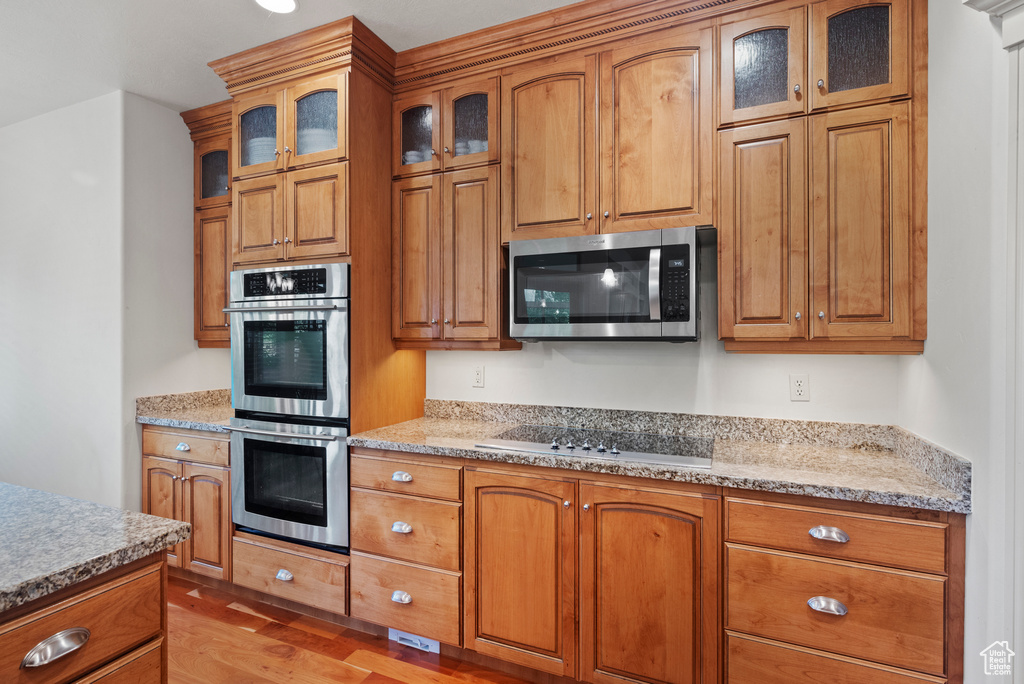 Kitchen featuring appliances with stainless steel finishes, brown cabinets, light wood finished floors, and light stone countertops