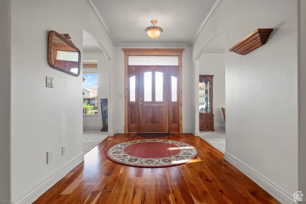 Foyer featuring arched walkways, wood finished floors, ornamental molding, and baseboards