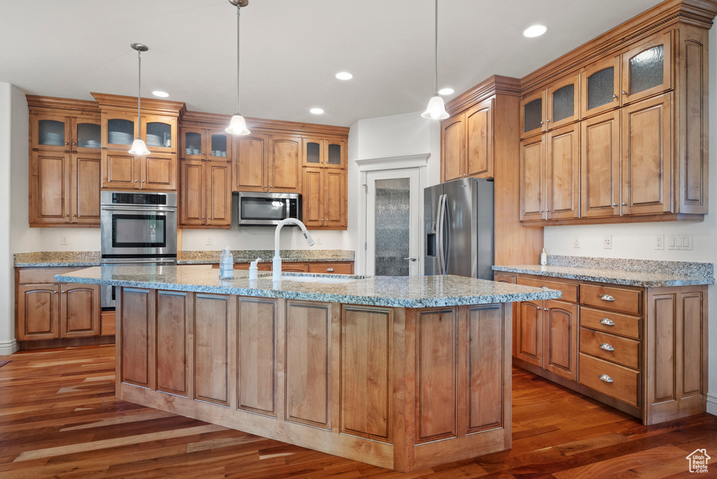 Kitchen with appliances with stainless steel finishes, wood finished floors, brown cabinets, a sink, and recessed lighting