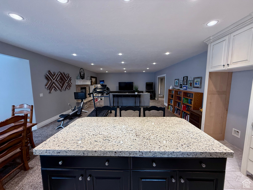 Kitchen with dark cabinetry, a center island, white cabinets, light stone counters, and recessed lighting