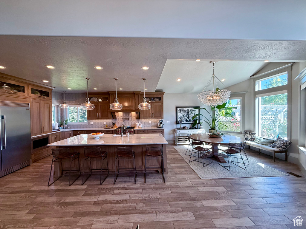 Kitchen featuring built in refrigerator, light countertops, a chandelier, a kitchen breakfast bar, and plenty of natural light