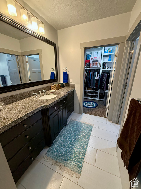 Bathroom with vanity, a walk in closet, a textured ceiling, and tile patterned flooring