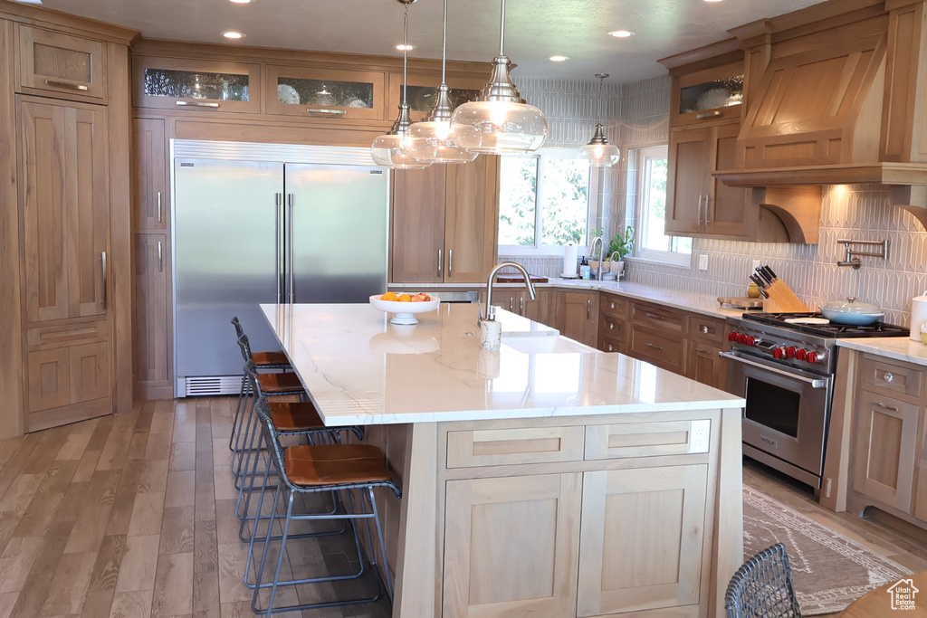 Kitchen with premium appliances, premium range hood, a sink, glass insert cabinets, and a kitchen bar