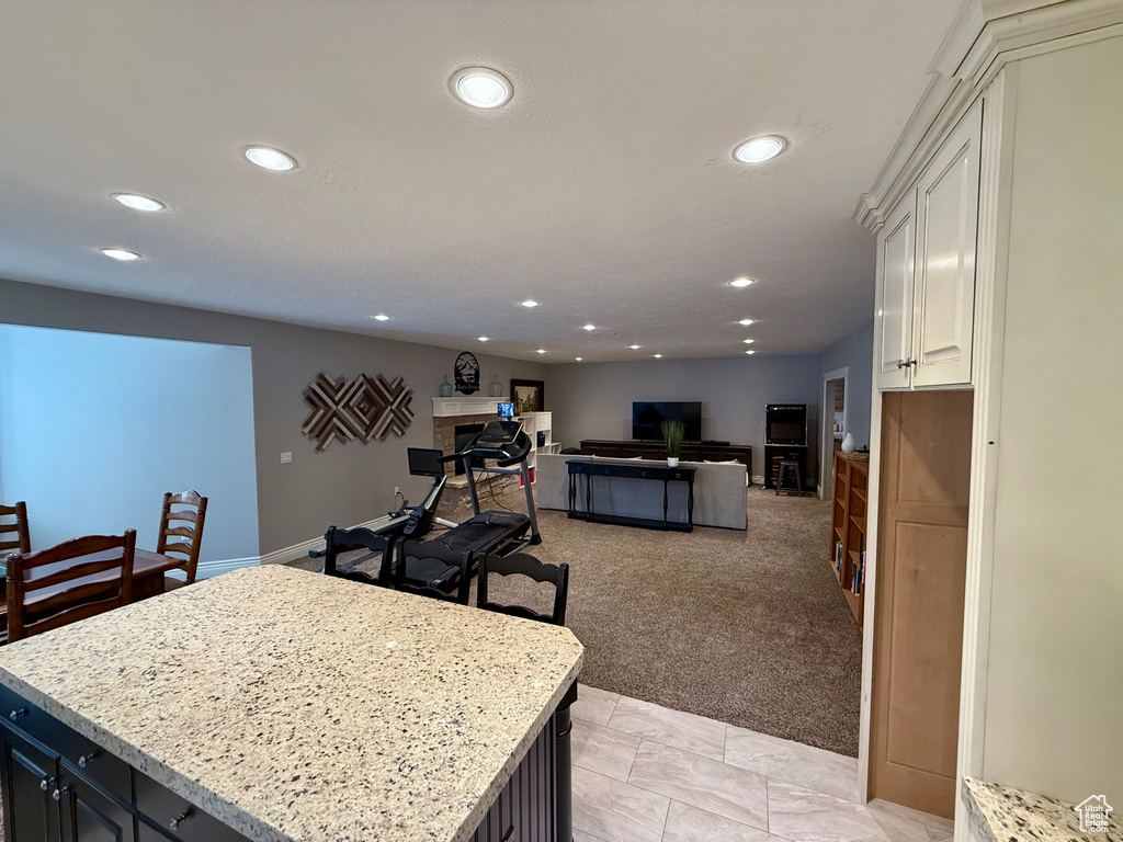 Kitchen with recessed lighting, a kitchen island, white cabinets, light stone counters, and light colored carpet