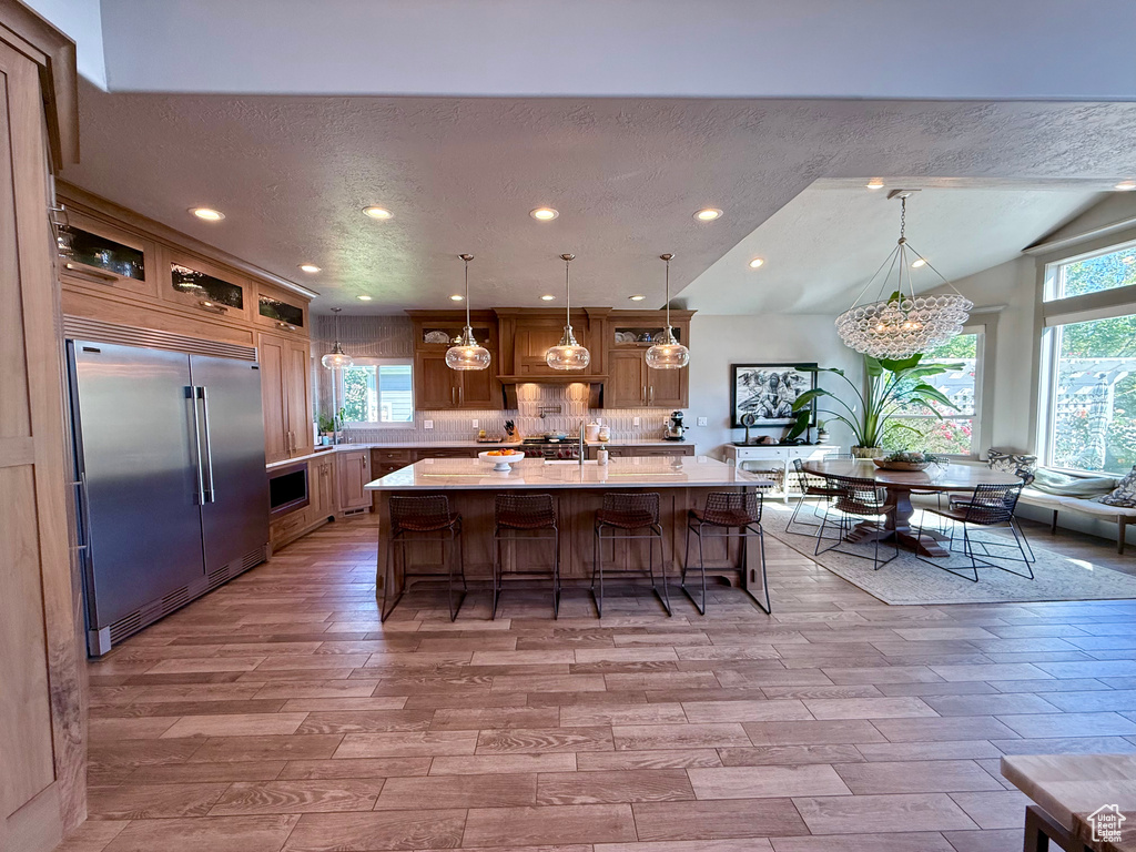 Kitchen featuring stainless steel built in refrigerator, light countertops, light wood-style floors, a breakfast bar area, and a center island with sink