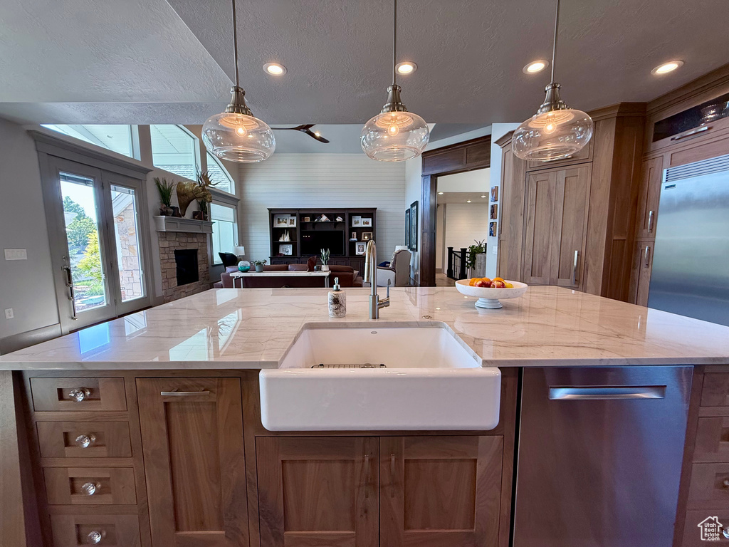 Kitchen with a sink, open floor plan, a fireplace, brown cabinets, and hanging light fixtures