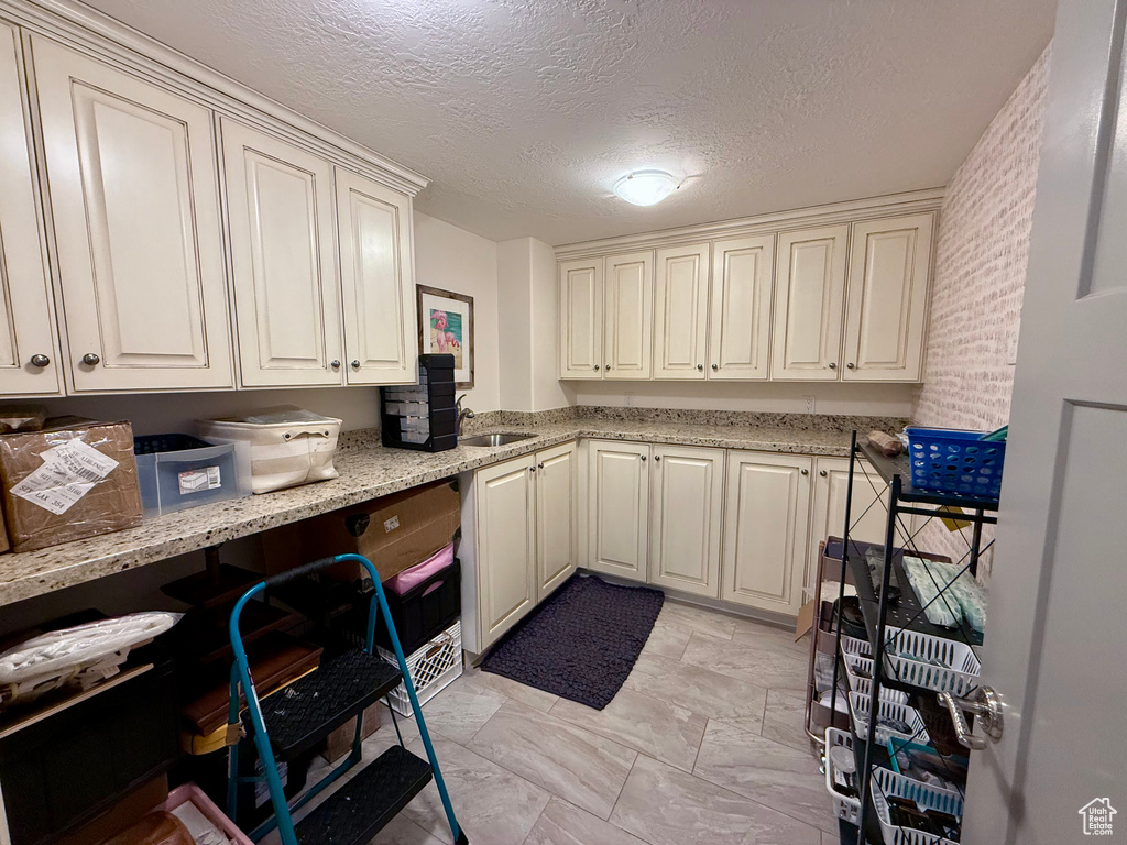 Kitchen with light stone countertops, a textured ceiling, a sink, and light marble finish floors