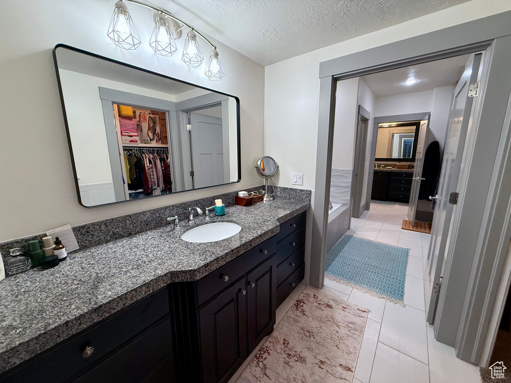 Bathroom with vanity, tile patterned flooring, a bath, a spacious closet, and a textured ceiling
