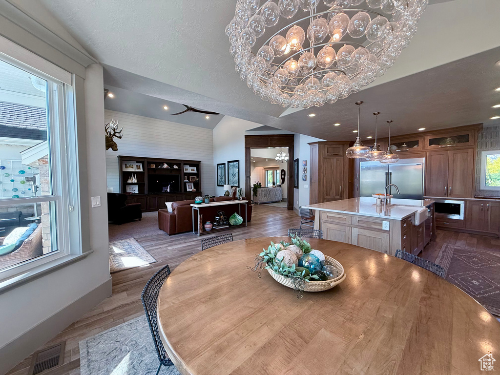 Dining space with wood finished floors, a chandelier, baseboards, recessed lighting, and lofted ceiling