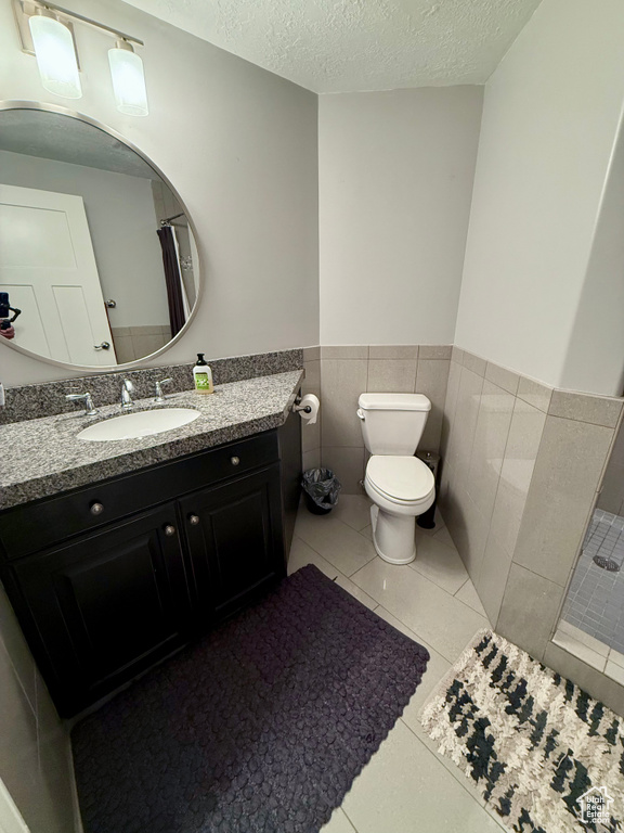 Bathroom featuring toilet, a textured ceiling, vanity, a wainscoted wall, and tile patterned flooring