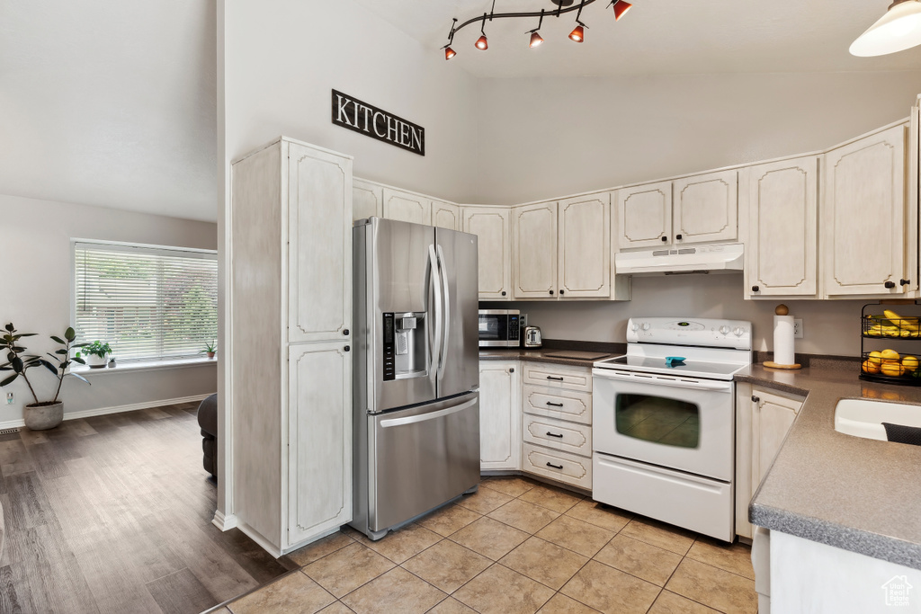 Kitchen featuring stainless steel appliances, high vaulted ceiling, under cabinet range hood, dark countertops, and light tile patterned flooring
