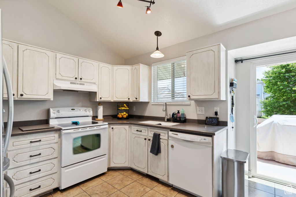Kitchen featuring white appliances, under cabinet range hood, dark countertops, a sink, and light tile patterned floors