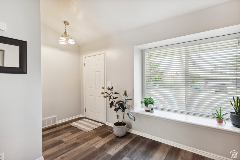 Foyer entrance with dark wood-style flooring, vaulted ceiling, baseboards, and a chandelier