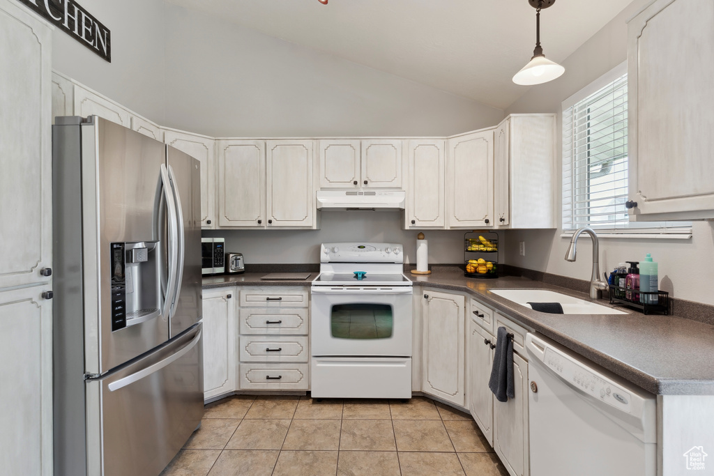 Kitchen with white appliances, under cabinet range hood, a sink, vaulted ceiling, and dark countertops