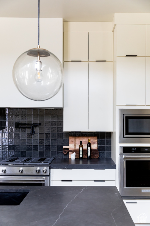 Kitchen featuring stainless steel appliances, dark countertops, modern cabinets, decorative backsplash, and white cabinetry