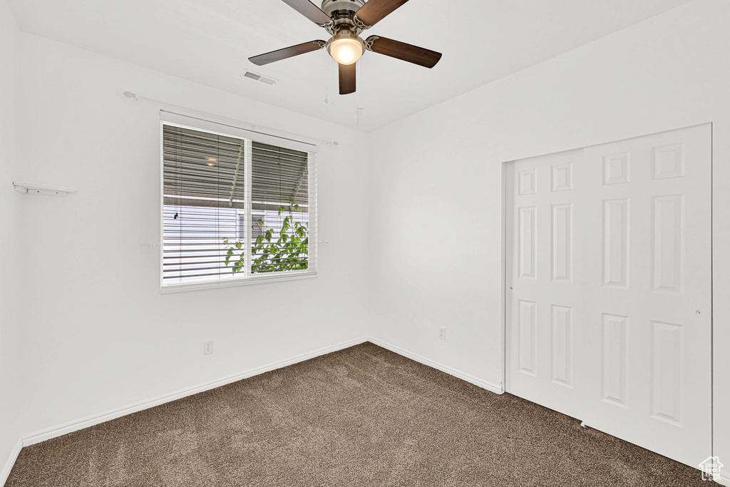 Unfurnished bedroom featuring dark colored carpet, baseboards, and ceiling fan