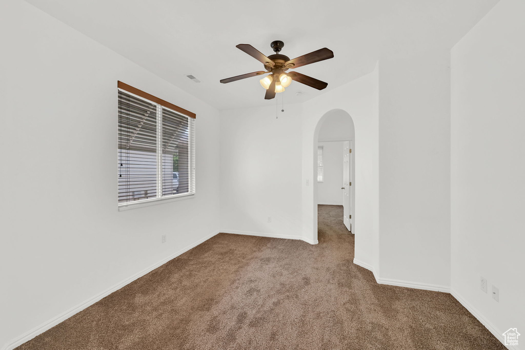 Unfurnished room with carpet floors, arched walkways, ceiling fan, and baseboards