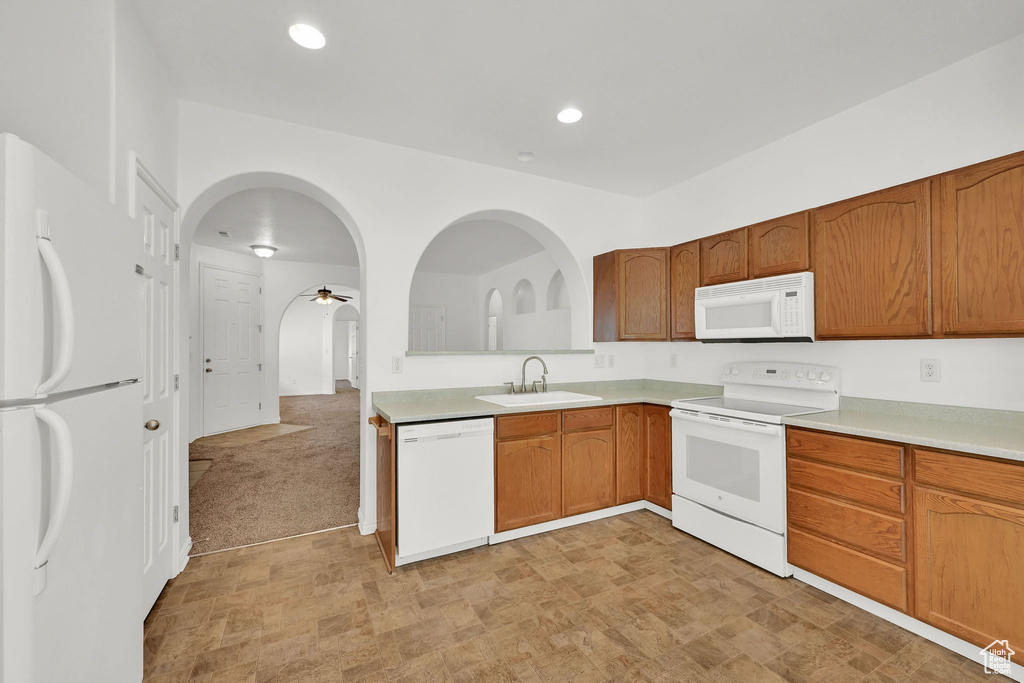 Kitchen featuring white appliances, a sink, light countertops, brown cabinetry, and recessed lighting