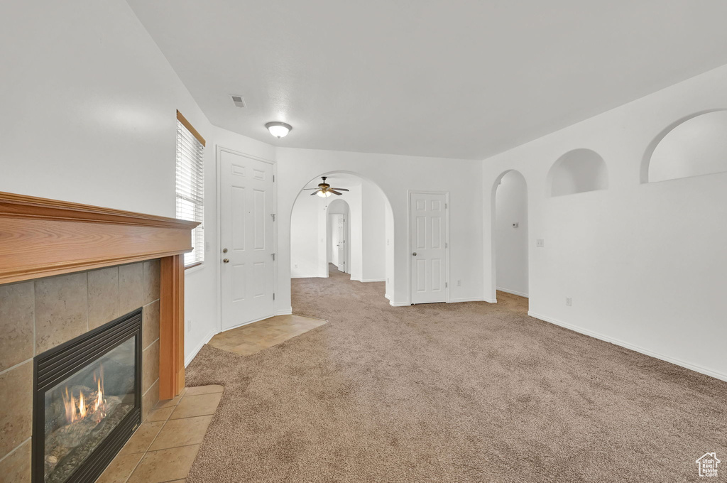 Unfurnished living room with arched walkways, a tile fireplace, light colored carpet, baseboards, and a ceiling fan