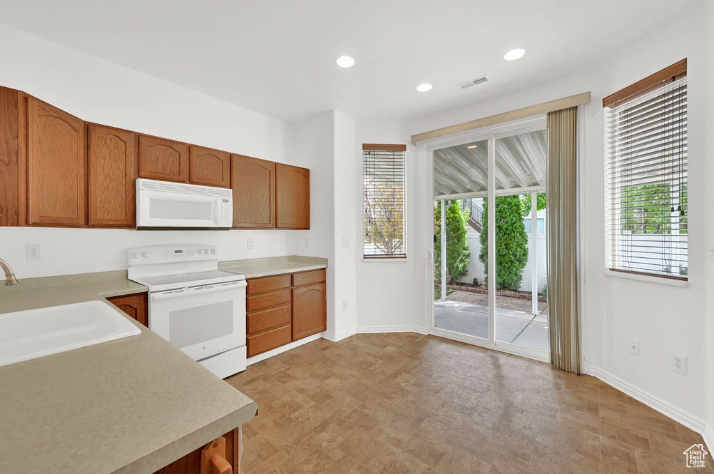 Kitchen with white appliances, a sink, baseboards, light countertops, and recessed lighting